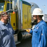 two Kimrad employees talking happily outside a yellow semi truck